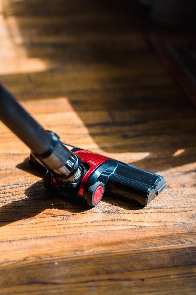 A high-angle view of a vacuum cleaner head working on a sunlit wooden floor.